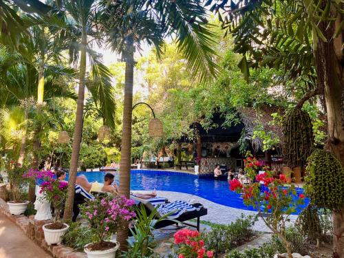 a swimming pool with palm trees and people sitting around it at Sundaras Sigiriya Jungles Caves Resort in Dambulla