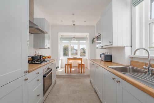 a kitchen with white cabinets and a sink and a table at Beaufort Heights by Grandeur Property in Iford