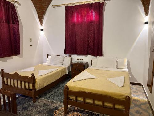 ルクソールにあるLuxor Villa Hatshepsutの赤いカーテンの部屋にベッドが2つある