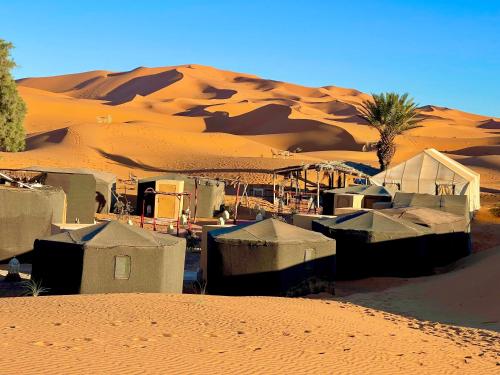 a group of tents in the desert with a sand mound at Moroccan Desert Camp in Merzouga
