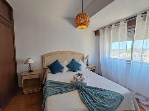 a bedroom with a bed with blue pillows and a window at 11A Rocha - Casas & Papeis in Armação de Pêra
