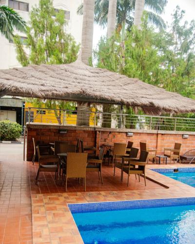 Un restaurante con una sombrilla de paja y sillas junto a una piscina. en Denis Hotel - Abuja, en Abuja