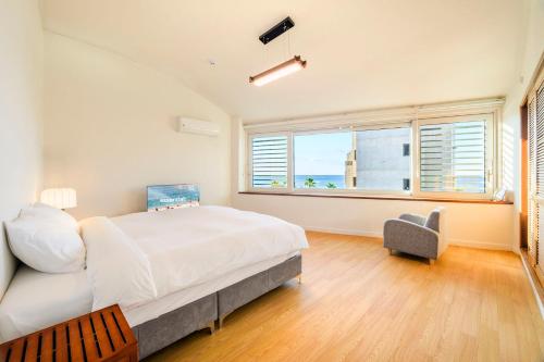 a bedroom with a bed and a chair and a window at Hold in Hamdeok with beach in Jeju