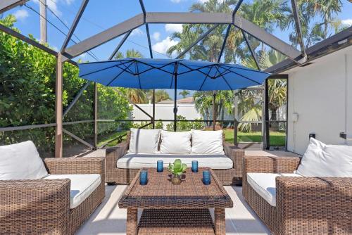 a patio with wicker furniture and a blue umbrella at Bimini Breeze - Updated Island Retreat with Pool & Beach Access in West Palm Beach