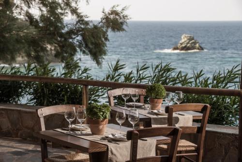 a table with wine glasses and potted plants and the ocean at Peninsula Resort & Spa in Agia Pelagia