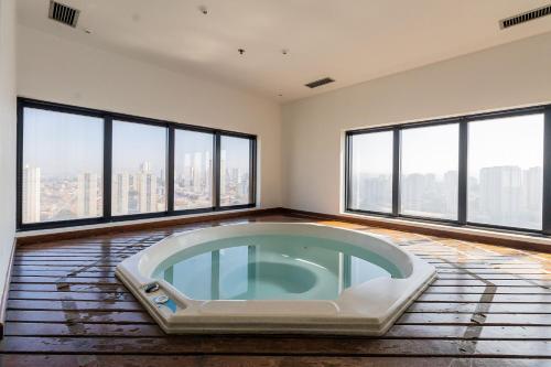 a hot tub in a room with large windows at Flat Hotel Slaviero GRU 2 Quartos até 6p | Delfhy in Vila Gopoúva