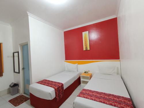 two beds in a room with a red wall at Hotel STIPRAM Kaliurang Yogyakarta in Kaliurang