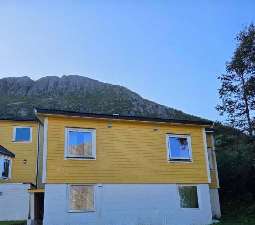a yellow house with a mountain in the background at Havblikk in Gryllefjord