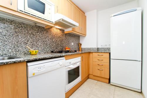 a kitchen with white appliances and wooden cabinets at Roura Planet Costa Dorada in La Pineda