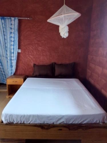 a bedroom with a white bed with a lamp on the wall at La Paillotte chez Ndoye in Ndayane