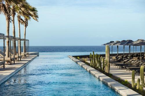 a pool at the beach with palm trees and chairs at Secrets Baby Beach Aruba Adults Only in Ceru Colorado