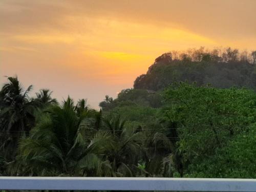 a sunset over a jungle with palm trees and a mountain at Sarvehuts Kashid in Kashid