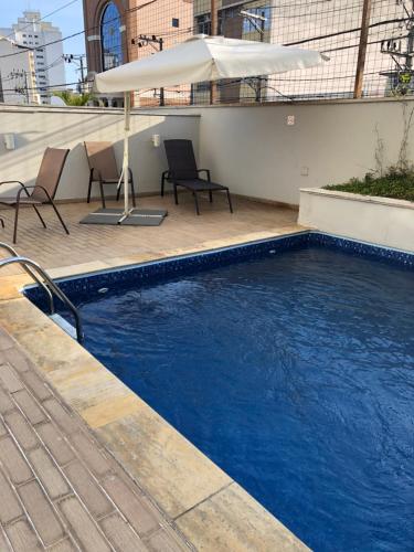 a large blue pool with chairs and an umbrella at Apart-Hotel Vila Mariana in Sao Paulo