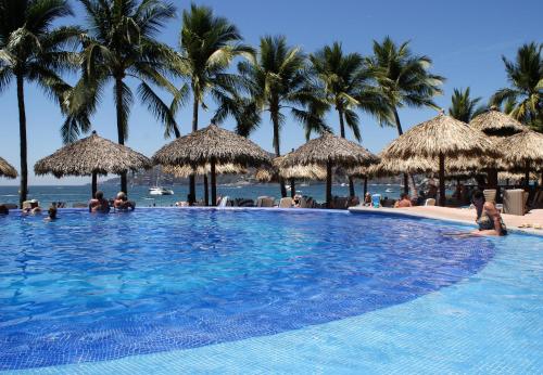 a large swimming pool with palm trees and the ocean at Hotel Villa Mexicana in Zihuatanejo