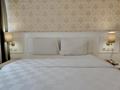 a bedroom with a white bed with two lamps and a wall at The Cube Hotel Malioboro, Azana Hotels Collection in Yogyakarta