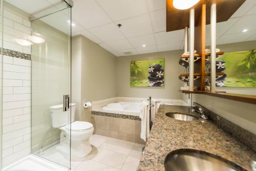 a bathroom with a sink and a tub and a toilet at Hôtel & Suites Le Dauphin Québec in Quebec City