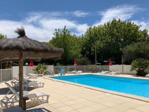 - une piscine avec un parasol et des chaises en paille à côté de la piscine dans l'établissement Mobil-home 30m² avec terrasse à Vendays-Montalivet - API-1-52-794, à Vendays-Montalivet