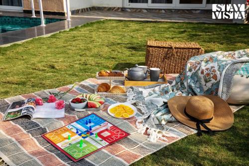 a picnic blanket with food and a hat on the grass at StayVista at Kankas House - BBQ & Bonfire in Jaipur