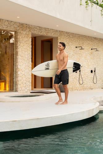 a man with a surfboard standing on a dock at Mira Hotel and Recovery in Uluwatu
