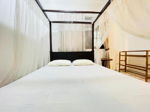 a bedroom with a white bed with white curtains at Dills Villa in Weligama