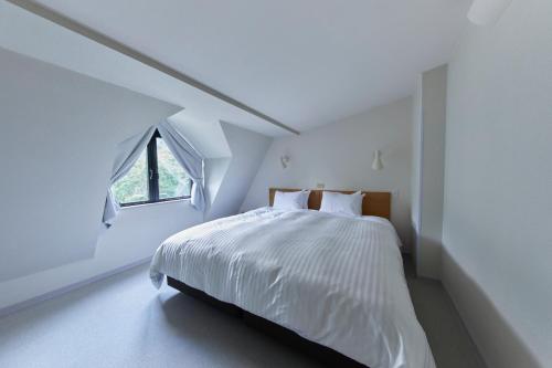 a white bedroom with a bed with a window at Hotel Stelle Belle in Hakuba