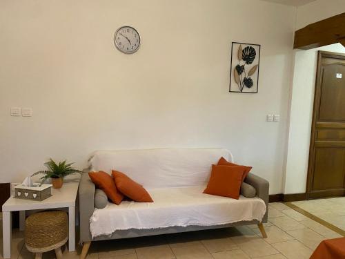 a white couch sitting in a living room with a clock on the wall at Gîte Bien Etre in Boulogne-sur-Gesse