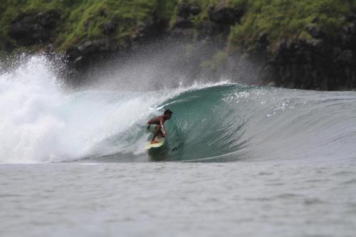 a man riding a wave on a surfboard in the ocean at My Beach House - Lombok - Kuta - Areguling beach in Kuta Lombok