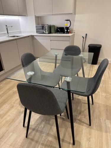a glass table with three chairs and a kitchen at Exquisite Riverview 2bedroom flat in Manchester. in Manchester