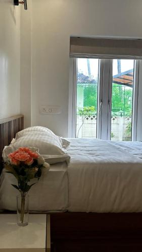 a white bed with a vase of flowers on a table at Vadanapilly Beach Villa for 8-10 adults in Irimbranallūr