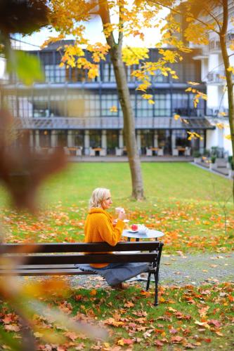 a woman sitting on a bench in a park at Hotel SPA Dr Irena Eris Polanica Zdrój in Polanica-Zdrój