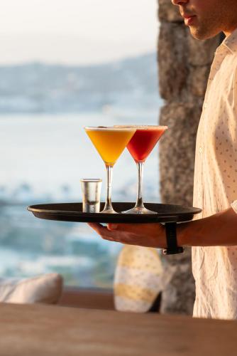 a woman holding a tray with two cocktails on it at Tharroe of Mykonos Boutique Hotel in Mýkonos City