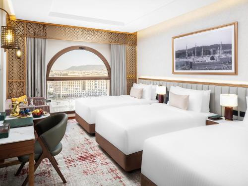 a hotel room with two beds and a desk at Elaf Taiba Hotel in Al Madinah