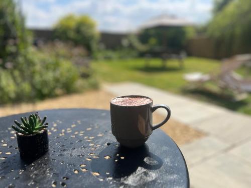 a black coffee cup sitting on a table with a plant at Private & Spacious Cotswold Barn in Hankerton