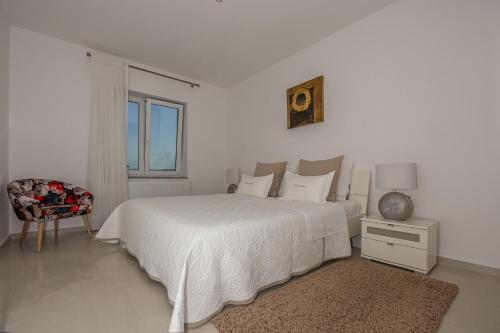 a white bedroom with a white bed and a chair at Apartments Villa Residenca in Novi Vinodolski