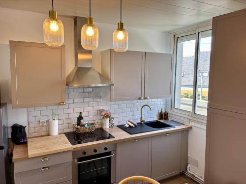 a kitchen with white cabinets and a sink and lights at Les Cocons d'Agathe, La Marinière, la plage à pieds in Larmor-Plage