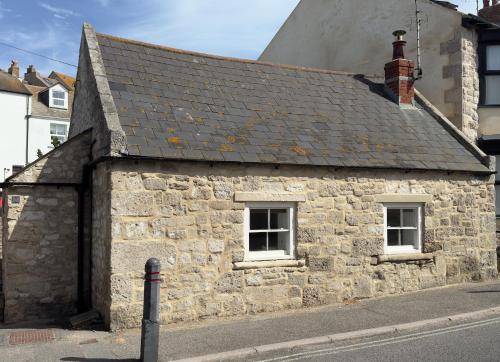 an old stone building with two windows on a street at Fisherman's Cottage on Chesil Beach in Castletown