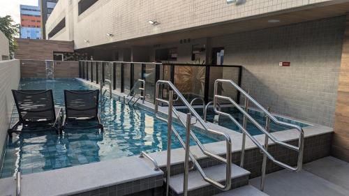 a swimming pool with chairs and stairs in a building at Studio Aconchegante 200m praia Pajuçara e P Verde in Maceió