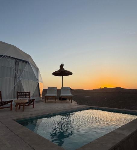 a tent with a pool and chairs and an umbrella at The Orion Dome in El Karia
