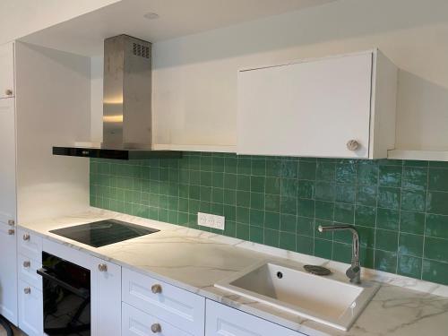 a kitchen with white cabinets and green tiles at Grande maison de charme in Enghien-les-Bains