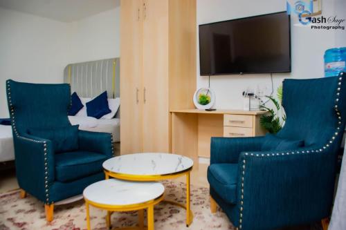 een woonkamer met blauwe stoelen, een tafel en een tv bij Haven 254 Stade view Suites in Nairobi