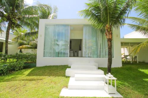 a white house with a palm tree in front of it at Pe na Areia Boutique Hotel in Japaratinga