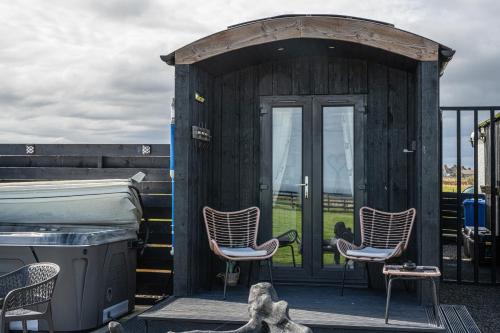 a small wooden cabin with three chairs on a deck at Hot Tub Haven Farr North 2 in Wick
