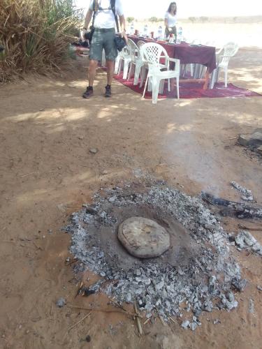 a man standing next to a fire pit on the beach at désert tours & Hôtel Titanic lac irik in Foum Zguid