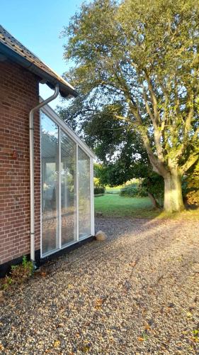 a glass greenhouse next to a brick house with a tree at Stately Apartment Incl Consumption in Bogense