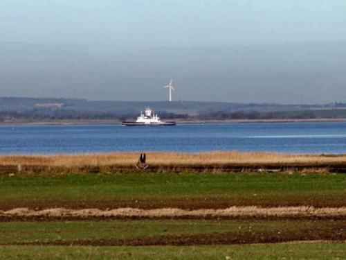 a boat on the water with a windmill in the distance at Scenic Retreat in Boddum - By Traum Ferienwohnungen in Boddum