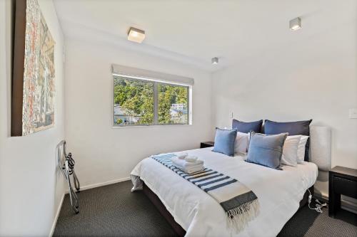 a white bedroom with a large bed with blue pillows at Paihia Beach 1 Bedroom Apartment in Paihia