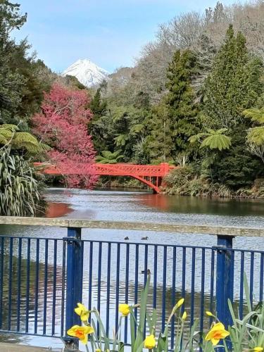a red bridge over a river with flowers in the foreground at Hill top view farm stay in Uruti