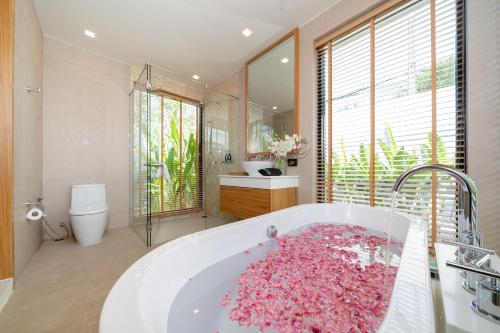 Un baño con una gran bañera llena de flores rosas. en Anchan Villas Phuket - 4 BR Signature Pool Villa by Escape Villas, en Ban Phru Champa