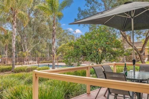 a deck with a table and chairs and an umbrella at Riverfront Escape - Pool Fun and Space for Everyone in Moama