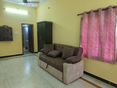 a living room with a couch and a pink curtain at Magizh Kudil - The House in Pūrnānkuppam